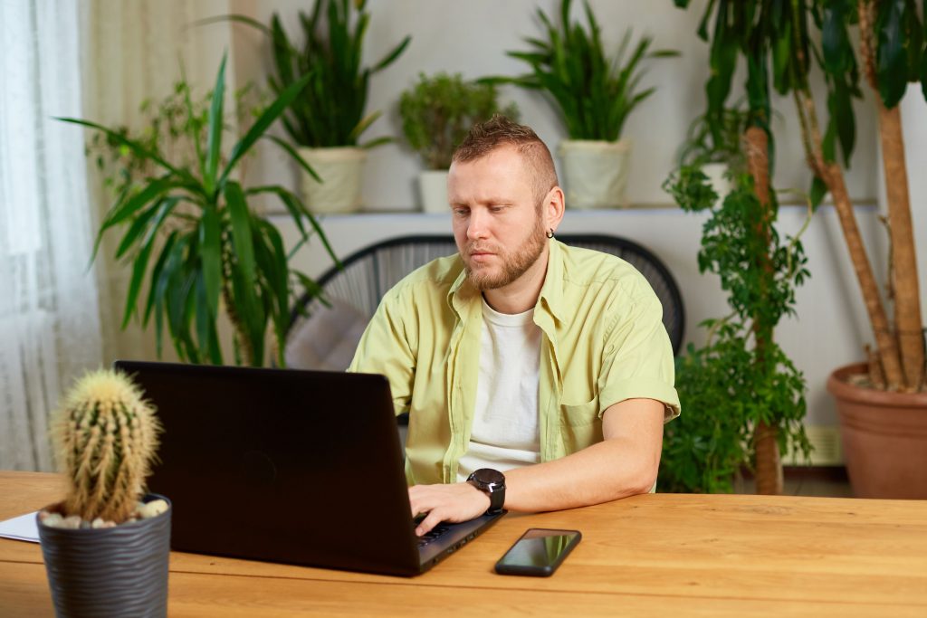 man typing on a laptop working from home and surrounded by plants