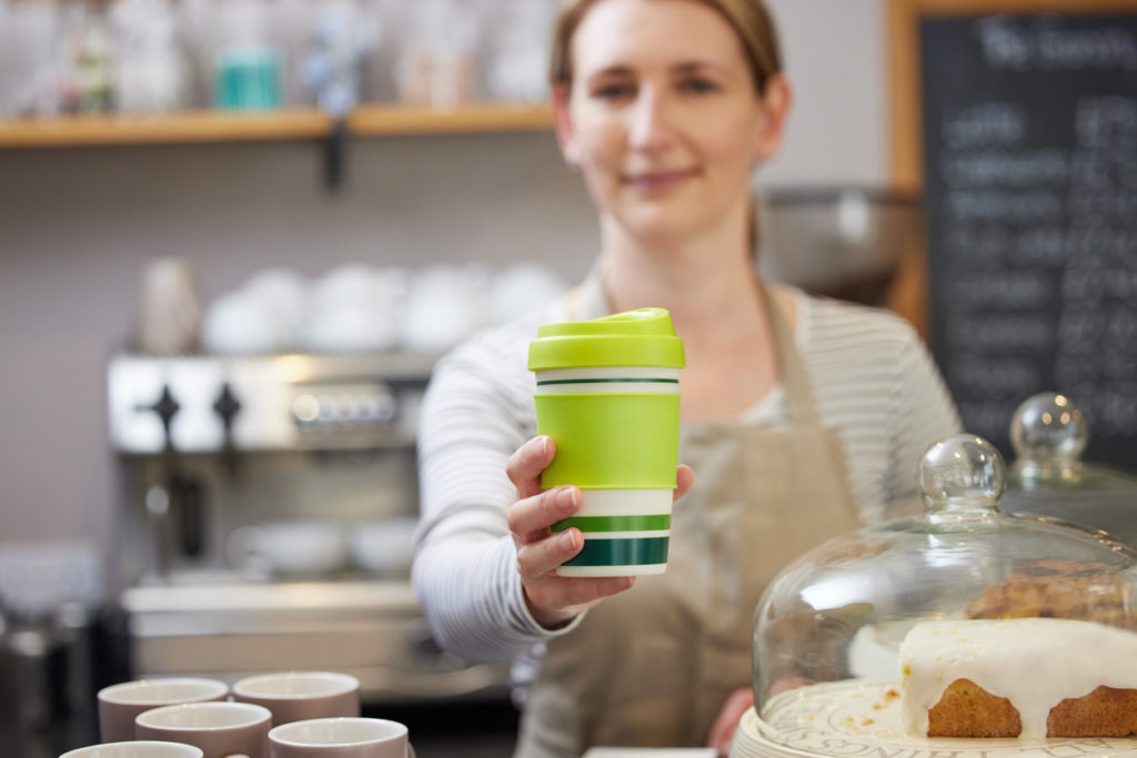 Female Worker in Cafe Serving Coffee In Sustainable Reusable Cup instead of a disposable paper cup