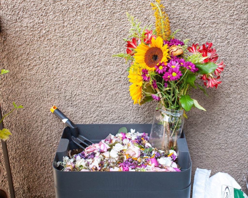 Flowers and petals being added to a compost bin.