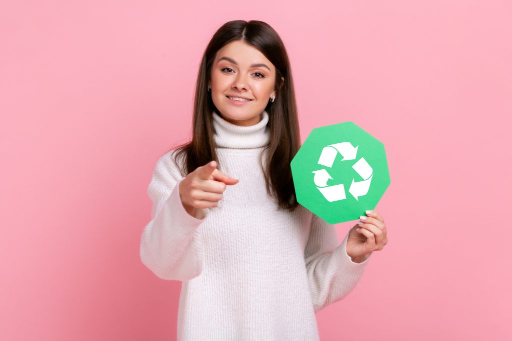 woman holding a recycling loop sign and pointing at the reader