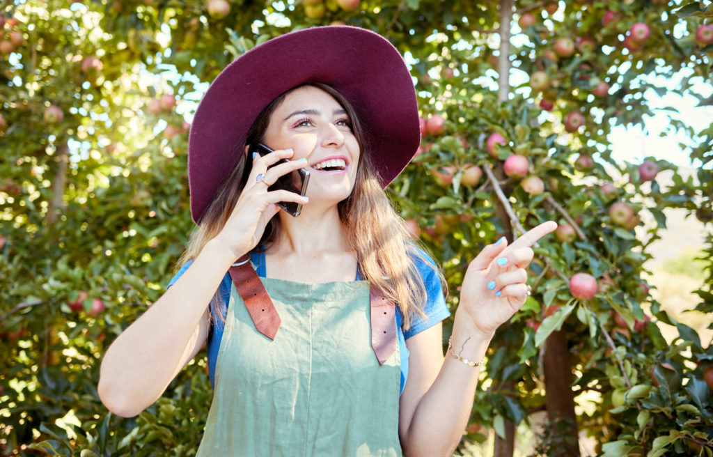 One happy woman talking on cellphone while working on sustainable apple orchard farm on sunny day. 