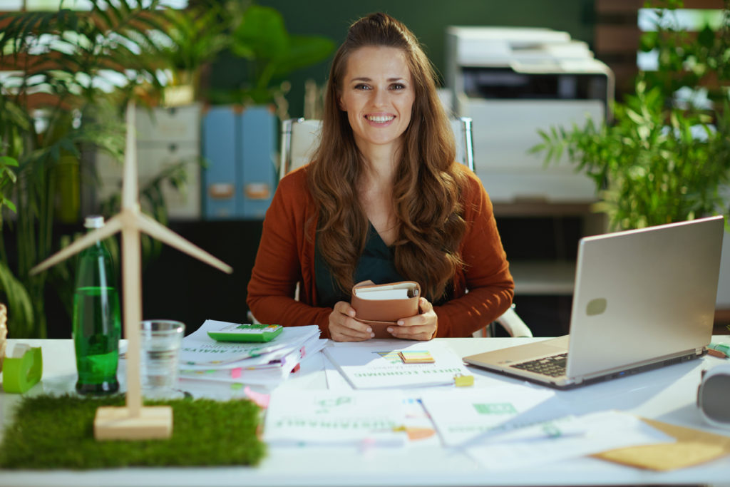 happy elegant middle aged small business owner woman with notebook and laptop in the modern green office.