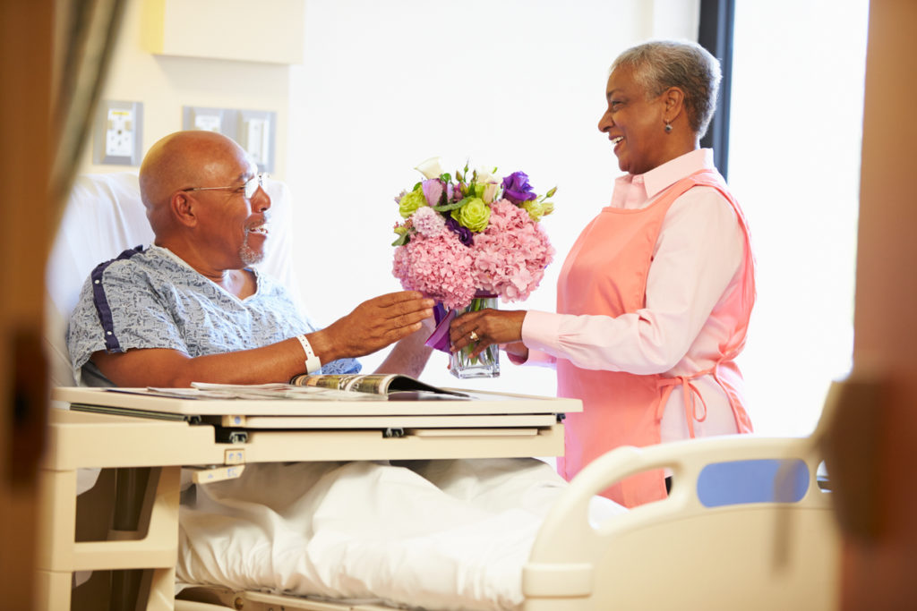 Volunteer Worker giving Male Patient flowers in his Hospital Room 