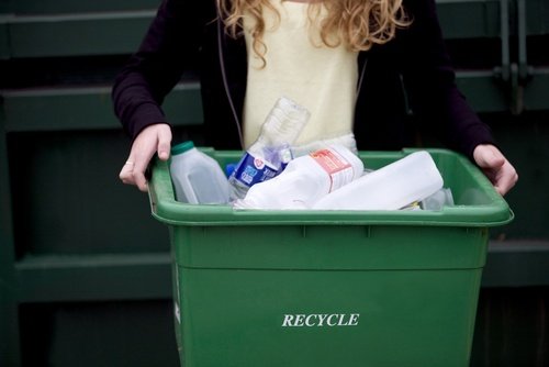 Girl holding green recycling bin with plastics inside of it