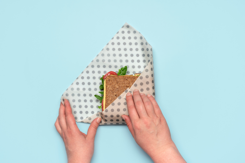 Hands folding beeswax food wrap around a sandwich