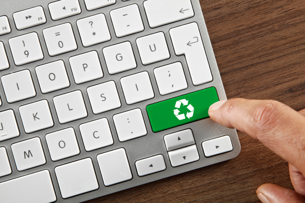 computer keyboard with an enter key that has been changed to a green key with a recycling loop on it. A finger is about to press the recycling key.