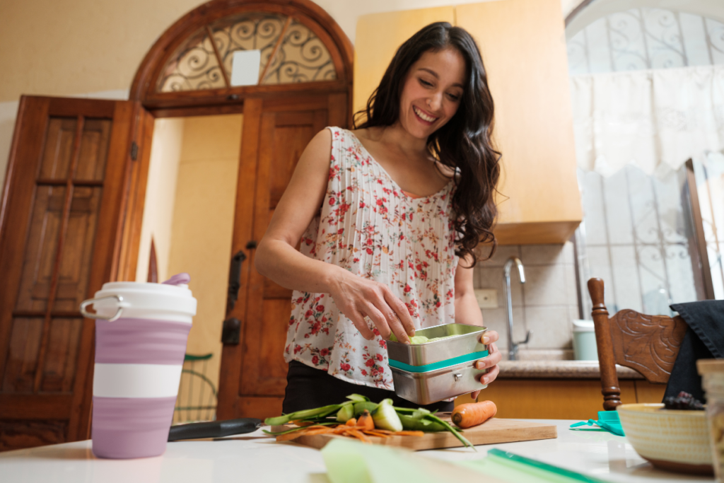 Woman packing her lunch into a reusable container. Reusable water bottle on the counter