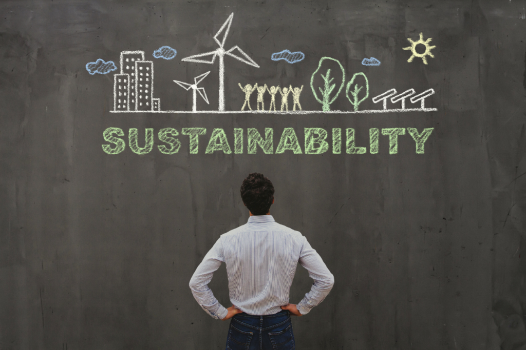 Business man looking at large chalkboard wall with chalk drawing of happy employees and sustainable technology with the word sustainability written underneath