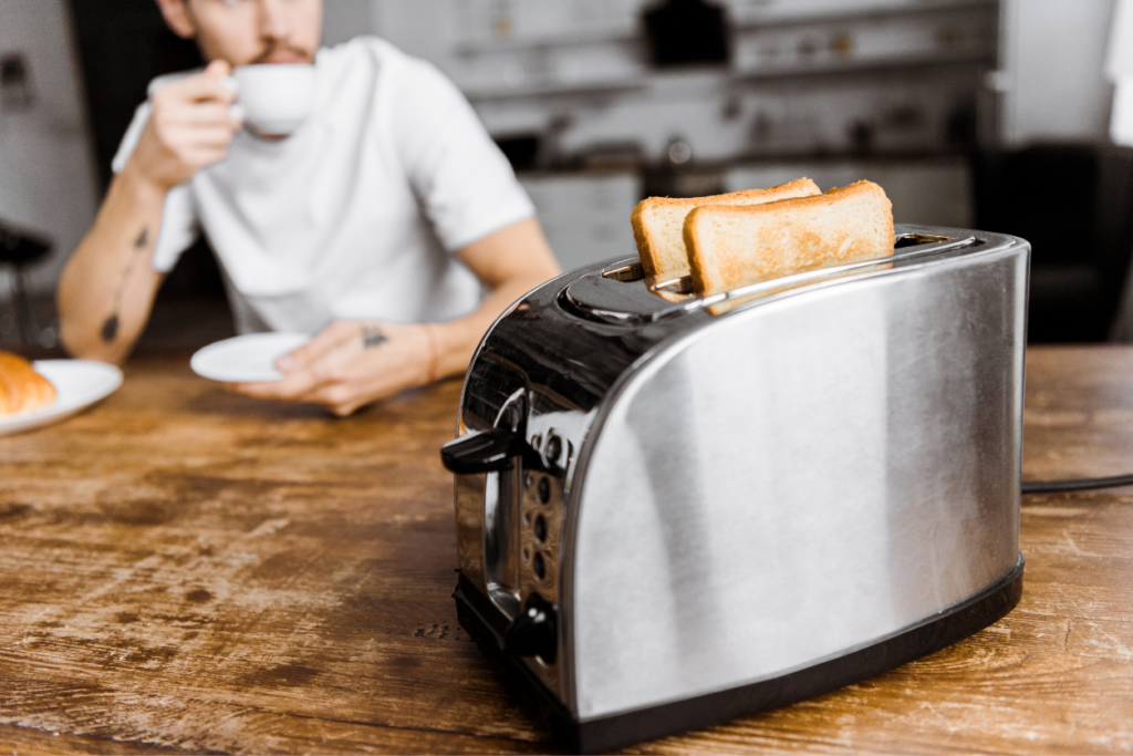 stainless steel toaster on wooden table with a man eating breakfast and drinking coffee in the background